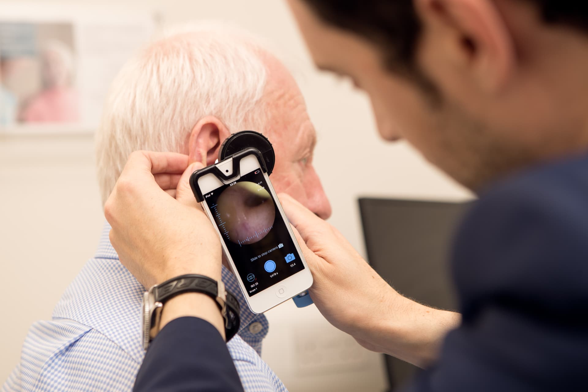 Audiologist examining a patient's ear canal with a video otoscope, the eardrum shown live on screen
