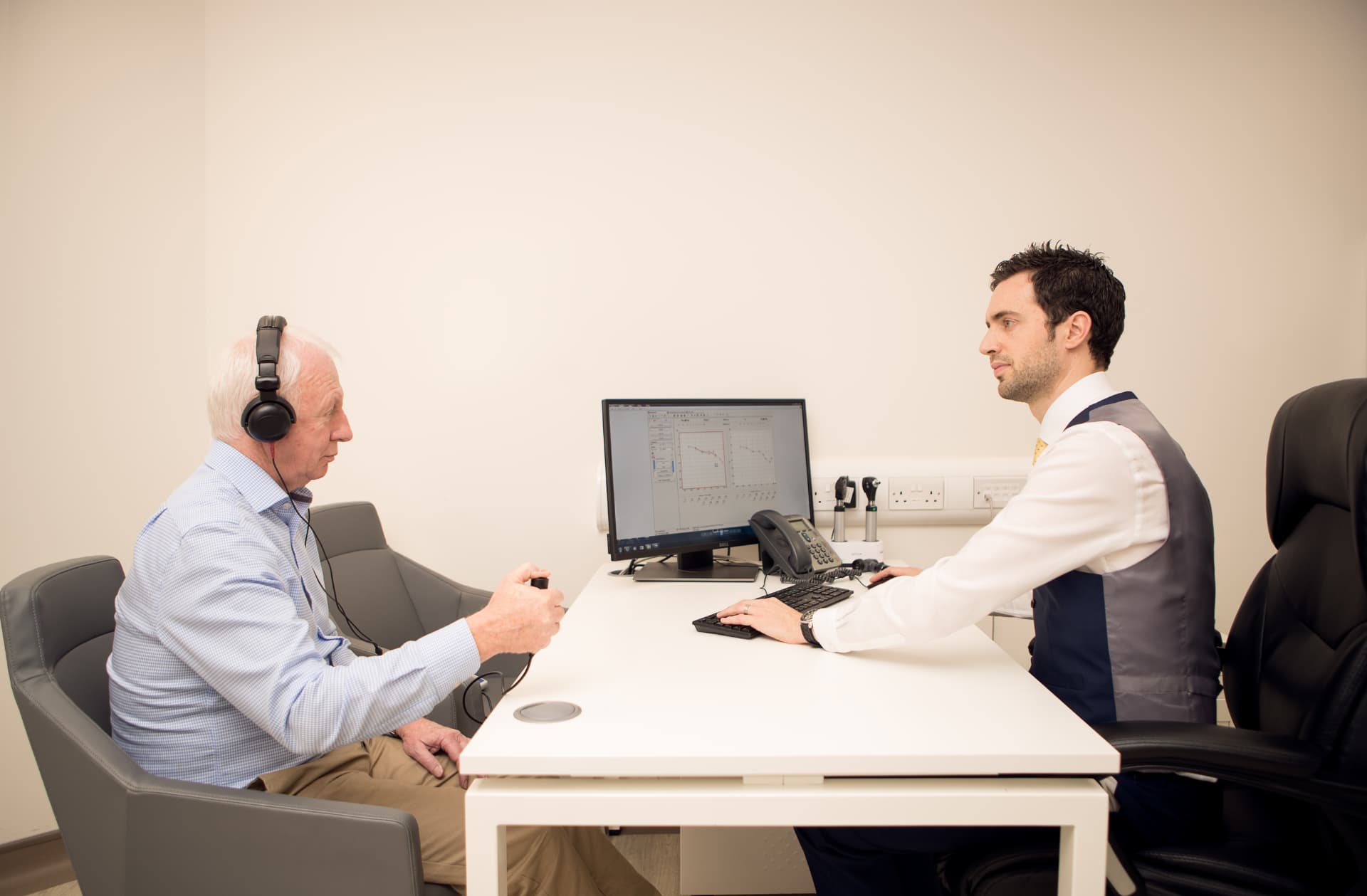 Audiologist and patient seated together in a Kensington clinic room with the audiogram results displayed on screen